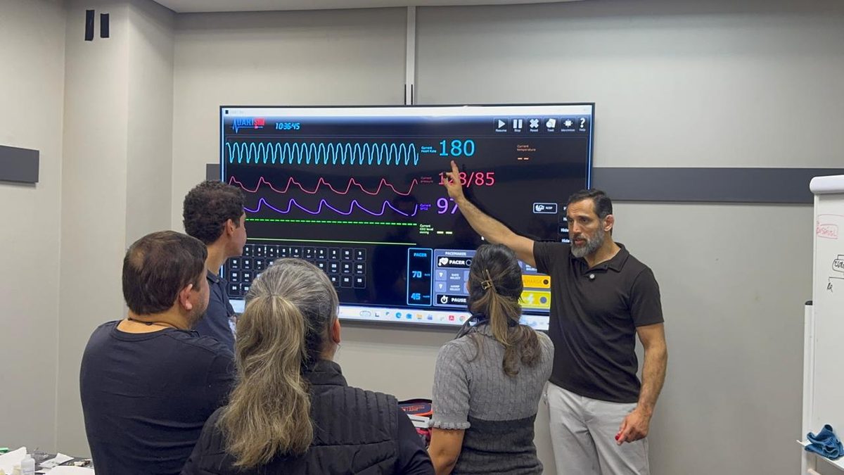 Prof. Marco Campos apontando para o monitor de simulação com o traçado de ritmo durante uma aula de ACLS